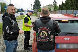 Zdjęcie przedstawia policjanta oraz motocyklistę rozmawiających z kierowcą samochodu.