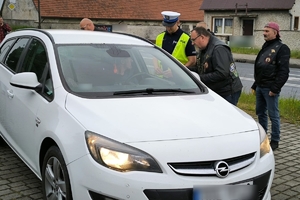 Zdjęcie przedstawia policjanta oraz motocyklistę rozmawiających z kierowcą samochodu.