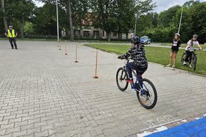 Zdjęcie przedstawia policjanta oraz dziecko pokonujące na rowerze tor przeszkód.