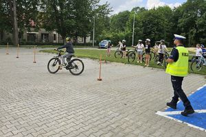 Zdjęcie przedstawia policjanta oraz dziecko pokonujące na rowerze tor przeszkód.