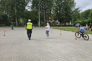 Zdjęcie przedstawia policjanta oraz dziecko pokonujące na rowerze tor przeszkód.