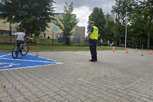 Zdjęcie przedstawia policjanta oraz dziecko pokonujące na rowerze tor przeszkód.