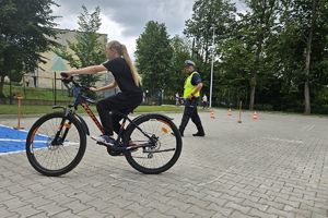 Zdjęcie przedstawia policjanta oraz dziecko pokonujące na rowerze tor przeszkód.