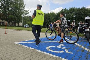 Zdjęcie przedstawia policjanta oraz dziecko pokonujące na rowerze tor przeszkód.