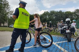 Zdjęcie przedstawia policjanta oraz dziecko pokonujące na rowerze tor przeszkód.