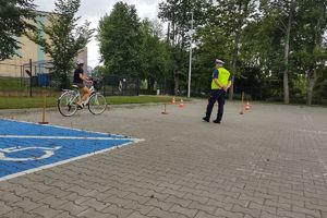 Zdjęcie przedstawia policjanta oraz dziecko pokonujące na rowerze tor przeszkód.