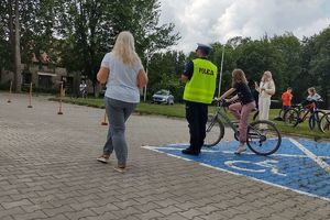 Zdjęcie przedstawia policjanta oraz dziecko pokonujące na rowerze tor przeszkód.