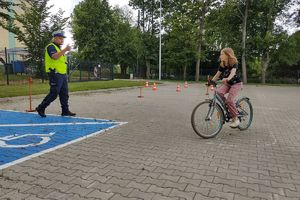 Zdjęcie przedstawia policjanta oraz dziecko pokonujące na rowerze tor przeszkód.