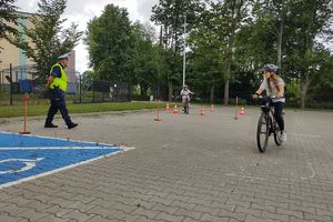 Zdjęcie przedstawia policjanta oraz dziecko pokonujące na rowerze tor przeszkód.