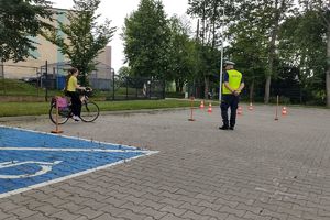 Zdjęcie przedstawia policjanta oraz dziecko pokonujące na rowerze tor przeszkód.