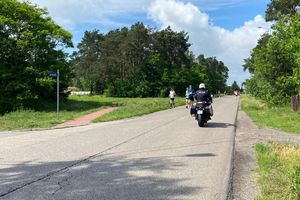 Zdjęcie przedstawia policyjny motocykl oraz biegaczy.