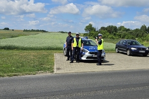 Zdjęcie przedstawia trzech policjantów, z których jeden trzyma radar oraz radiowóz.