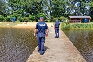 dwóch umundurowanych policjantów idzie po molo na zbiorniku wodnym, obserwują okolicę