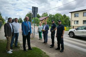 umundurowani policjanci wraz innymi osobami stoją na chodniku przy drodze