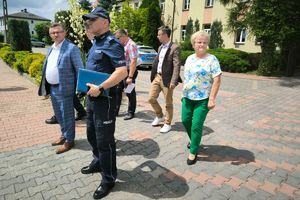 umundurowany policjant wraz innymi osobami stoi na chodniku przy drodze