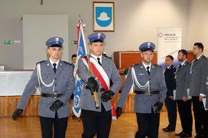 Zdjęcie przedstawia umundurowanych policjantów maszerujących ze sztandarem.