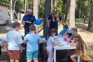 Policjant i policjantka stoją przy stołach, przy których siedzą dzieci