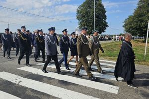 Zdjęcie przedstawia maszerujących uczestników obchodów, w tym policjantów.