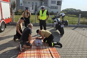 Zdjęcie przedstawia policjanta, strażaków ochotników, mężczyznę przy fantomie.