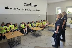 Zdjęcie przedstawia policjantki oraz dzieci w kamizelkach odblaskowych podczas prelekcji.