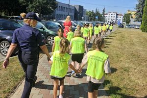 Zdjęcie przedstawia grupę dzieci w kamizelkach odblaskowych oraz policjantki idących chodnikiem.