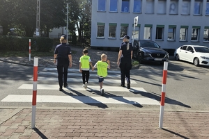 Zdjęcie przedstawia policjantki oraz dzieci w kamizelkach odblaskowych na przejściu dla pieszych.