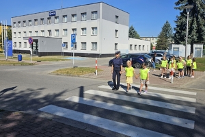 Zdjęcie przedstawia policjantkę oraz dzieci w kamizelkach odblaskowych na przejściu dla pieszych.