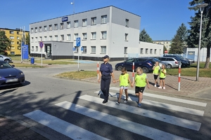 Zdjęcie przedstawia policjantkę oraz dzieci w kamizelkach odblaskowych na przejściu dla pieszych.