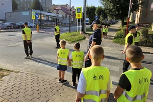 Zdjęcie przedstawia uczniów oraz policjantki przechodzących przez oznakowane przejście dla pieszych.