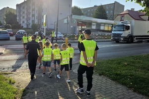 Zdjęcie przedstawia uczniów oraz policjantki przechodzących przez oznakowane przejście dla pieszych.