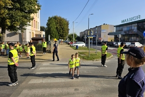 Zdjęcie przedstawia uczniów oraz policjantki przechodzących przez oznakowane przejście dla pieszych.