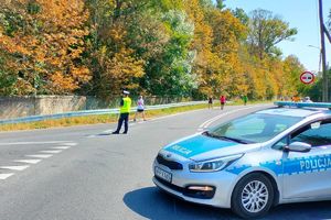 Zdjęcie przedstawia policjanta, radiowóz oraz uczestników biegu.