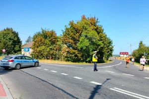 Zdjęcie przedstawia policjanta, radiowóz oraz uczestników biegu.