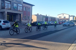 Zdjęcie przedstawia grupę rowerzystów w kamizelkach odblaskowych oraz policyjny radiowóz.