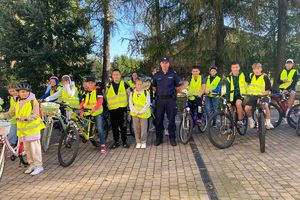 Zdjęcie przedstawia policjanta oraz grupę rowerzystów w kamizelkach odblaskowych.