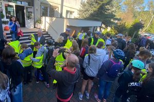 Zdjęcie przedstawia policjantów rozdających kamizelki odblaskowe grupie dzieci.