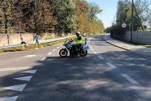 Zdjęcie przedstawia policjanta na motocyklu oraz biegaczy.