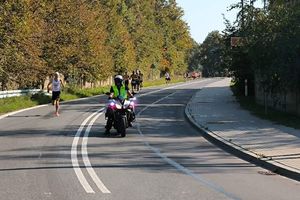 Zdjęcie przedstawia policjanta na motocyklu oraz biegaczy.