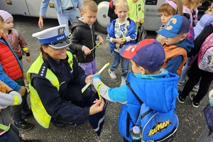 Zdjęcie przedstawia policjantkę, która zakłada chłopcu na rękę opaskę odblaskową.