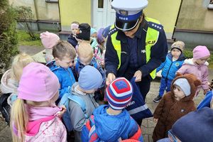 Zdjęcie przedstawia policjantkę rozdającą odblaski przedszkolakom.