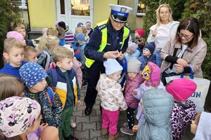 Zdjęcie przedstawia policjantkę rozdającą odblaski przedszkolakom.