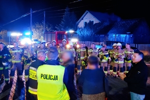 Zdjęcie przedstawia policjantów, strażaków, odnalezionych grzybiarzy oraz radiowóz i wóz strażacki.