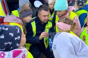 Zdjęcie przedstawia policjanta oraz dzieci w kamizelkach odblaskowych.