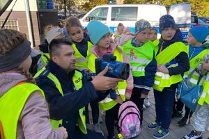 Zdjęcie przedstawia policjanta oraz dzieci w kamizelkach odblaskowych.