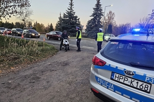 Zdjęcie przedstawia radiowóz, dwóch policjantów oraz motocyklistę zatrzymanego do kontroli.