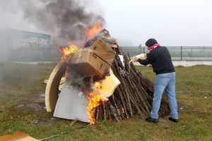 Zdjęcie przedstawia mężczyznę lejącego ciecz na ognisko.