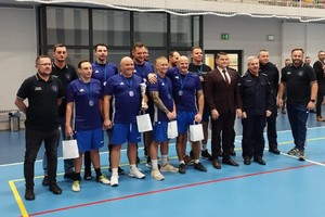 na zdjęciu widać drużynę męską siatkówki ubraną w stroje sportowe, obok stoją umundurowani policjanci oraz inne osoby