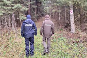 Zdjęcie przedstawia policjanta i strażnika leśnego na drodze leśnej.