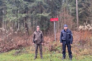 Zdjęcie przedstawia policjanta i strażnika leśnego na drodze leśnej.