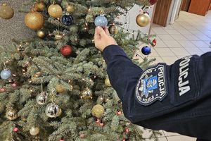 Zdjęcie przedstawia rękę policjanta w mundurze, który wiesza bombkę na choince.